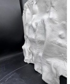 Close view of a white clay study with deep vertical folds like draped fabric, on a black ground.